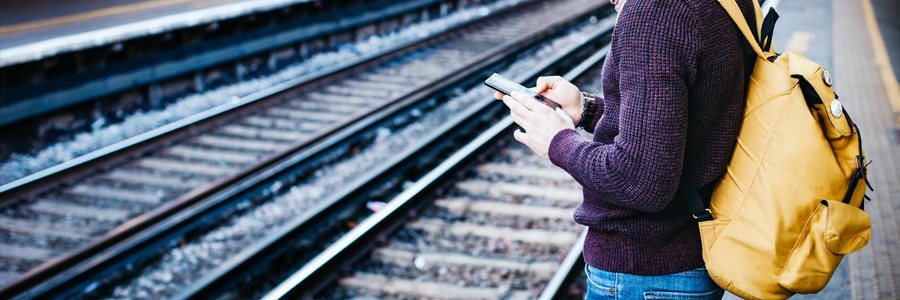 Young man holding cell phone beside train tracks. Public transportation accidents in Toronto. Contact Conte and Associates, personal injury lawyers, in Whitby and Vaughan.