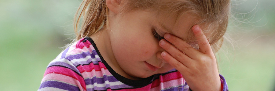 Little girl holding head in pain. Help prevent head injury in children.